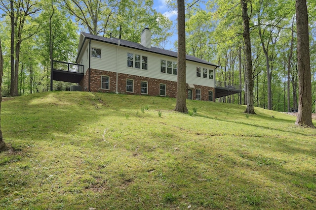 back of house with a chimney, central air condition unit, a lawn, a deck, and brick siding