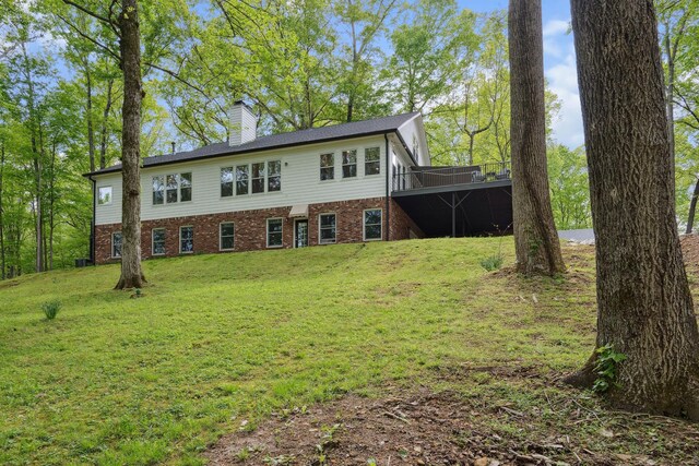 rear view of house with brick siding, a yard, a chimney, and a deck