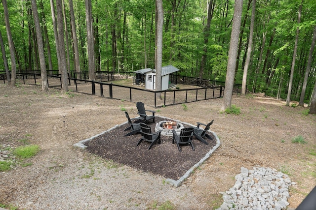 view of yard featuring a fenced backyard, a fire pit, a view of trees, an outdoor structure, and a shed