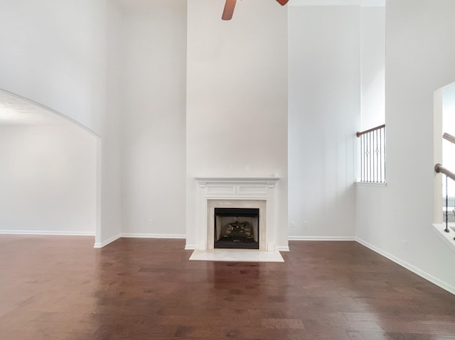 unfurnished living room featuring a fireplace with flush hearth, a high ceiling, a ceiling fan, and wood finished floors