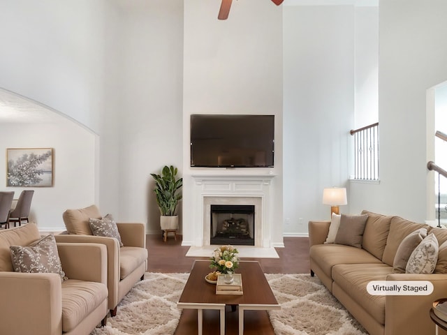 living room featuring ceiling fan, wood finished floors, a towering ceiling, and a fireplace