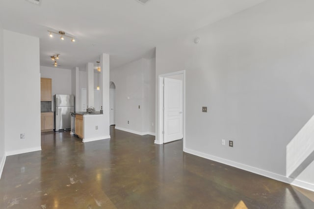unfurnished living room with a sink, baseboards, arched walkways, and finished concrete floors