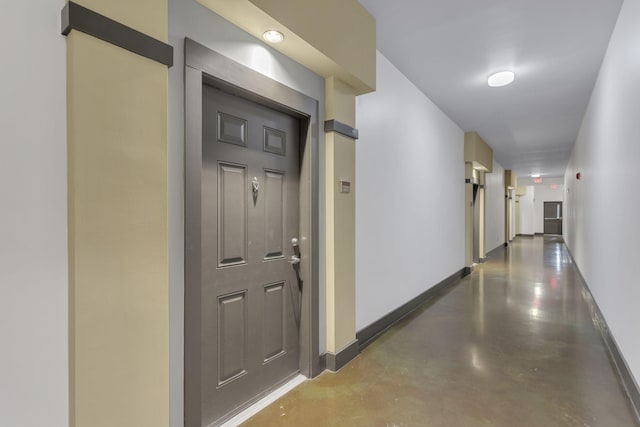 hall featuring finished concrete flooring and baseboards