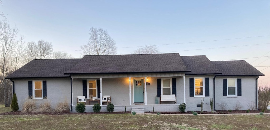 single story home featuring roof with shingles, a porch, and a front yard