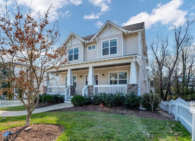 craftsman-style home featuring board and batten siding, a front lawn, fence, a porch, and stone siding