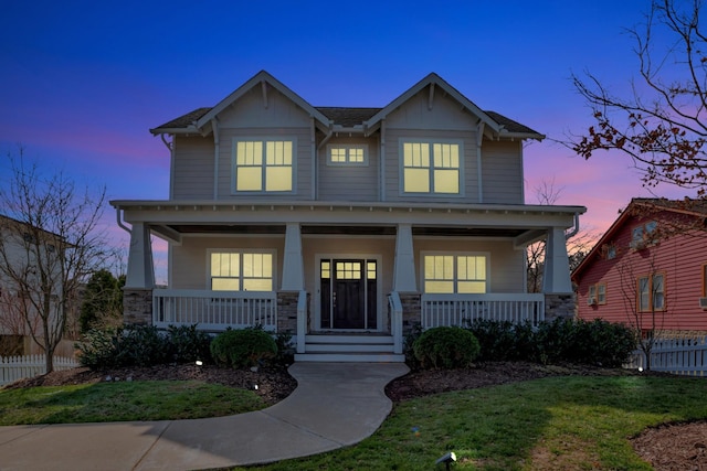 craftsman-style house with a front yard, fence, covered porch, and stone siding