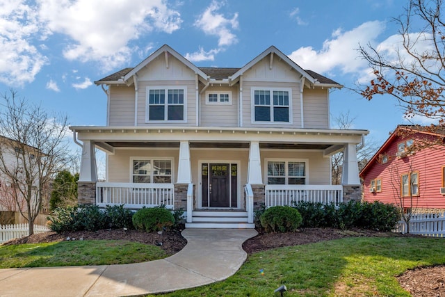 craftsman-style home featuring a front yard, fence, covered porch, and stone siding