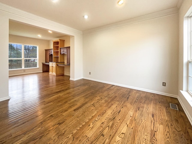 unfurnished living room featuring visible vents, baseboards, dark wood-type flooring, and crown molding