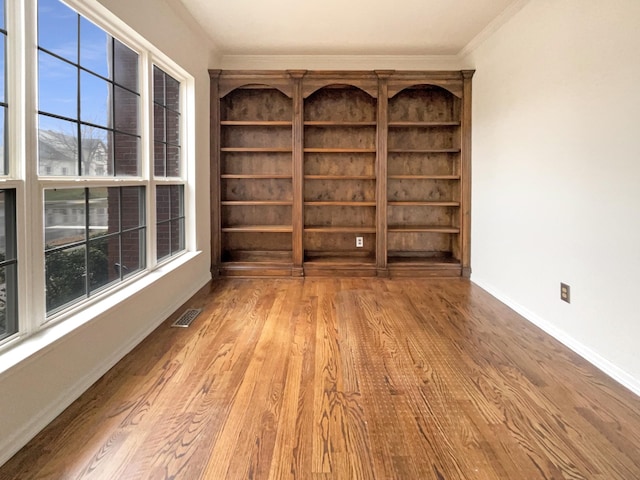 empty room featuring visible vents, crown molding, baseboards, and wood finished floors