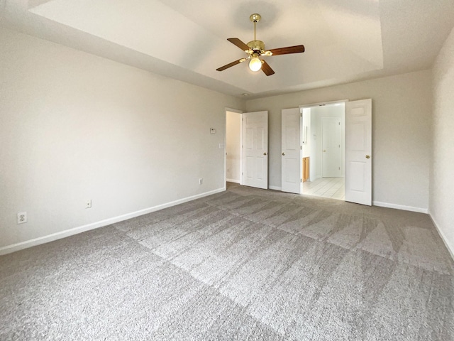 unfurnished bedroom featuring ensuite bathroom, baseboards, a tray ceiling, and carpet