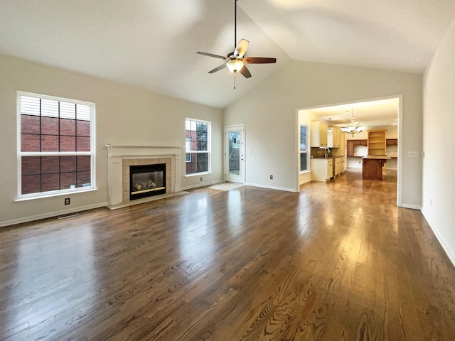 unfurnished living room with baseboards, a fireplace, dark wood-style flooring, vaulted ceiling, and ceiling fan with notable chandelier