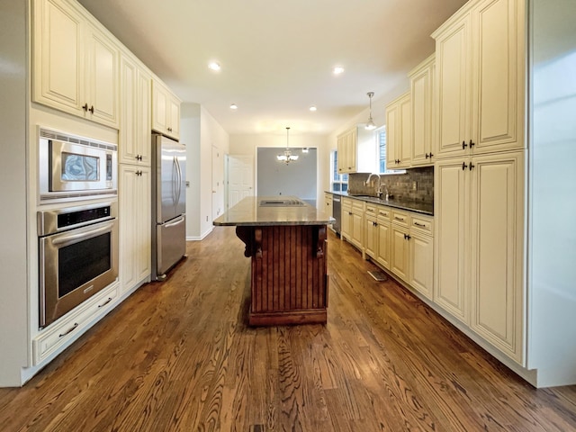 kitchen featuring a kitchen island, decorative backsplash, appliances with stainless steel finishes, dark wood-style floors, and a sink