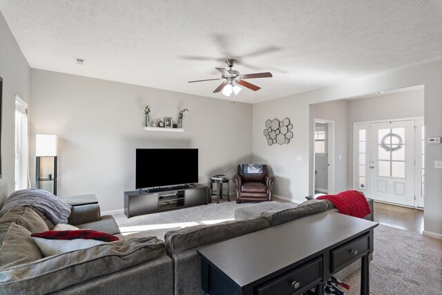 carpeted living room with visible vents, baseboards, a textured ceiling, and a ceiling fan