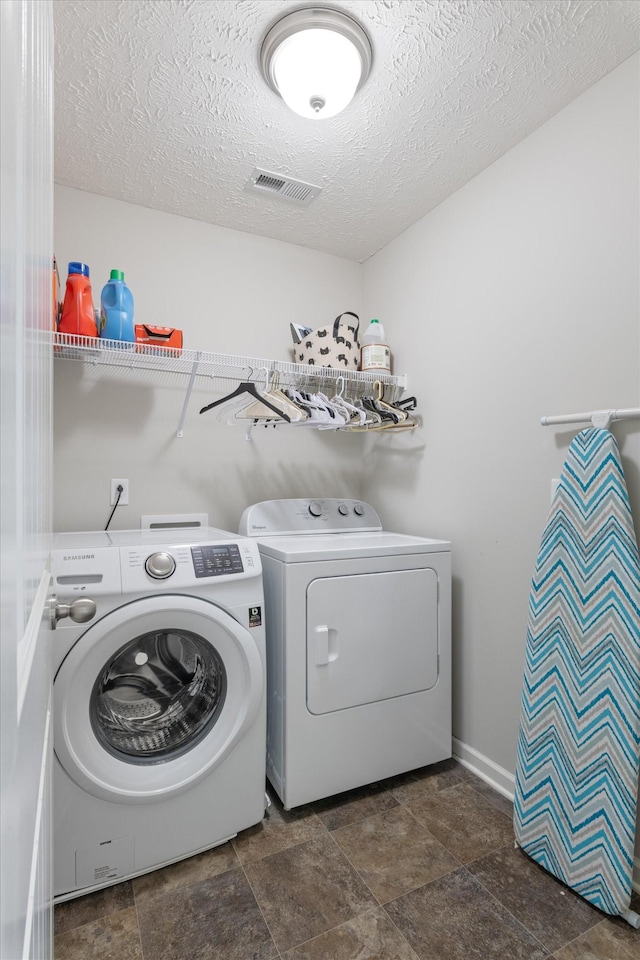 laundry room featuring visible vents, washer and dryer, stone finish flooring, a textured ceiling, and laundry area