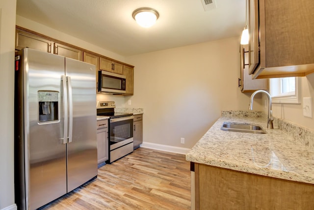 kitchen featuring visible vents, a sink, stainless steel appliances, light wood-style floors, and brown cabinetry