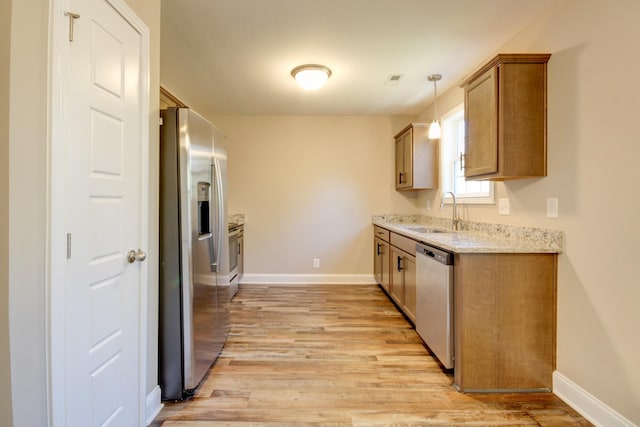 kitchen with light wood finished floors, brown cabinets, appliances with stainless steel finishes, and a sink