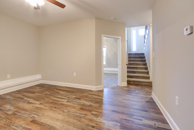 unfurnished room with a ceiling fan, stairway, wood finished floors, and baseboards