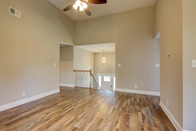 spare room with wood finished floors, visible vents, baseboards, a high ceiling, and ceiling fan with notable chandelier