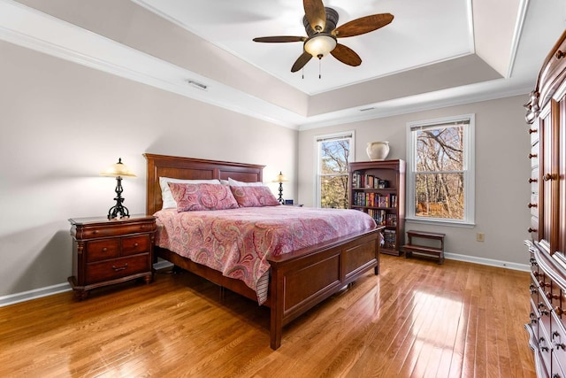 bedroom with visible vents, a tray ceiling, light wood-style floors, crown molding, and baseboards