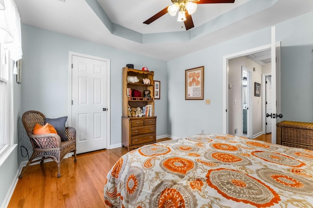 bedroom featuring light wood-style flooring, baseboards, a tray ceiling, and ceiling fan