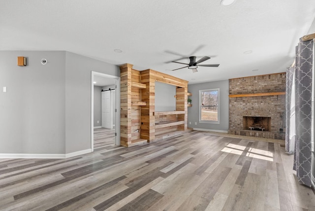 928 Red Bird Ln, Cumberland Furnace, TN 37051 - unfurnished living room with a ceiling fan, wood finished floors, a barn door, a fireplace, and baseboards