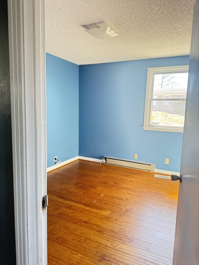 unfurnished room with visible vents, baseboards, baseboard heating, wood finished floors, and a textured ceiling