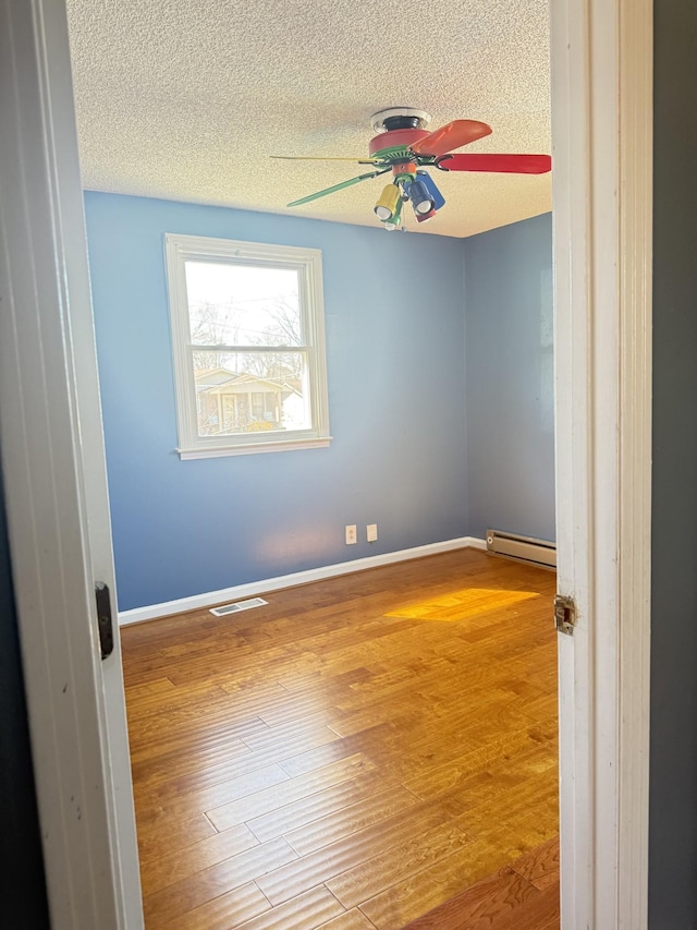 unfurnished room with a baseboard radiator, baseboards, a textured ceiling, and wood finished floors