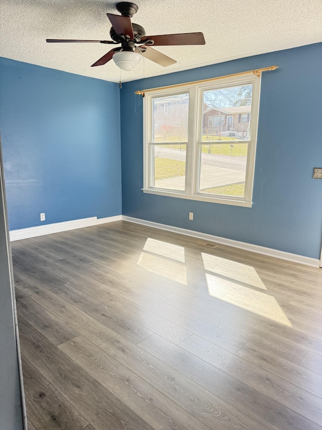 empty room with ceiling fan, baseboards, a textured ceiling, and wood finished floors