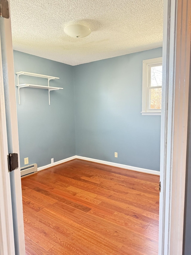 empty room with a textured ceiling, wood finished floors, baseboards, and a baseboard radiator