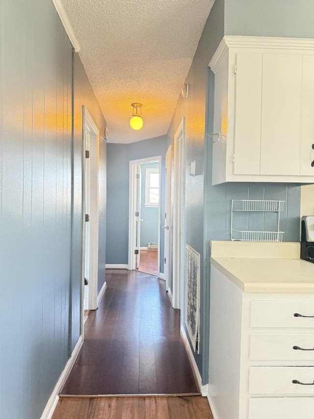 corridor featuring dark wood-style floors, visible vents, a textured ceiling, and baseboards