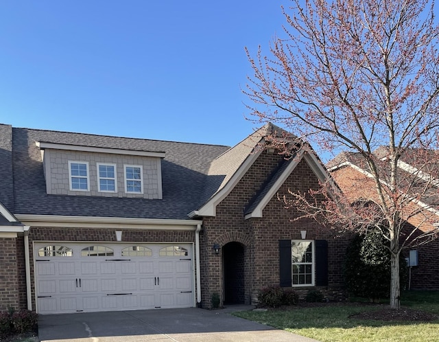 view of front of house with a front yard, driveway, a shingled roof, a garage, and brick siding