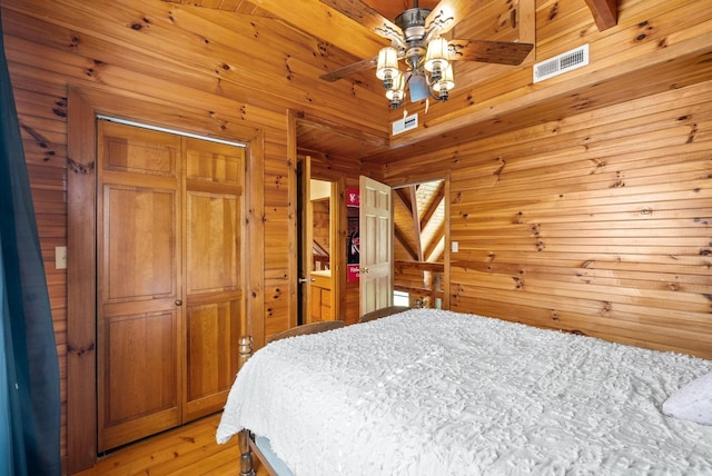 bedroom featuring visible vents, wood walls, wooden ceiling, light wood-style floors, and a closet