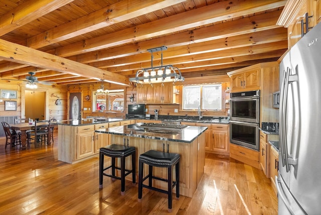 kitchen featuring a center island, beam ceiling, light wood-style flooring, a peninsula, and stainless steel appliances