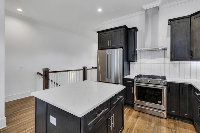 kitchen featuring ornamental molding, wood finished floors, appliances with stainless steel finishes, wall chimney range hood, and decorative backsplash