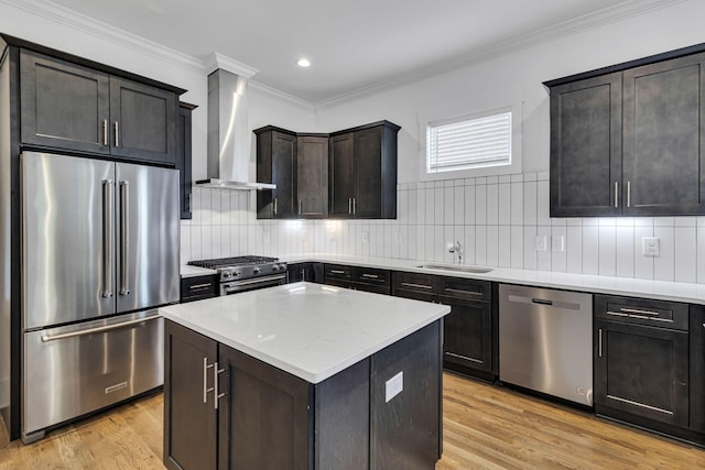 kitchen with light wood finished floors, high quality appliances, wall chimney exhaust hood, and a sink