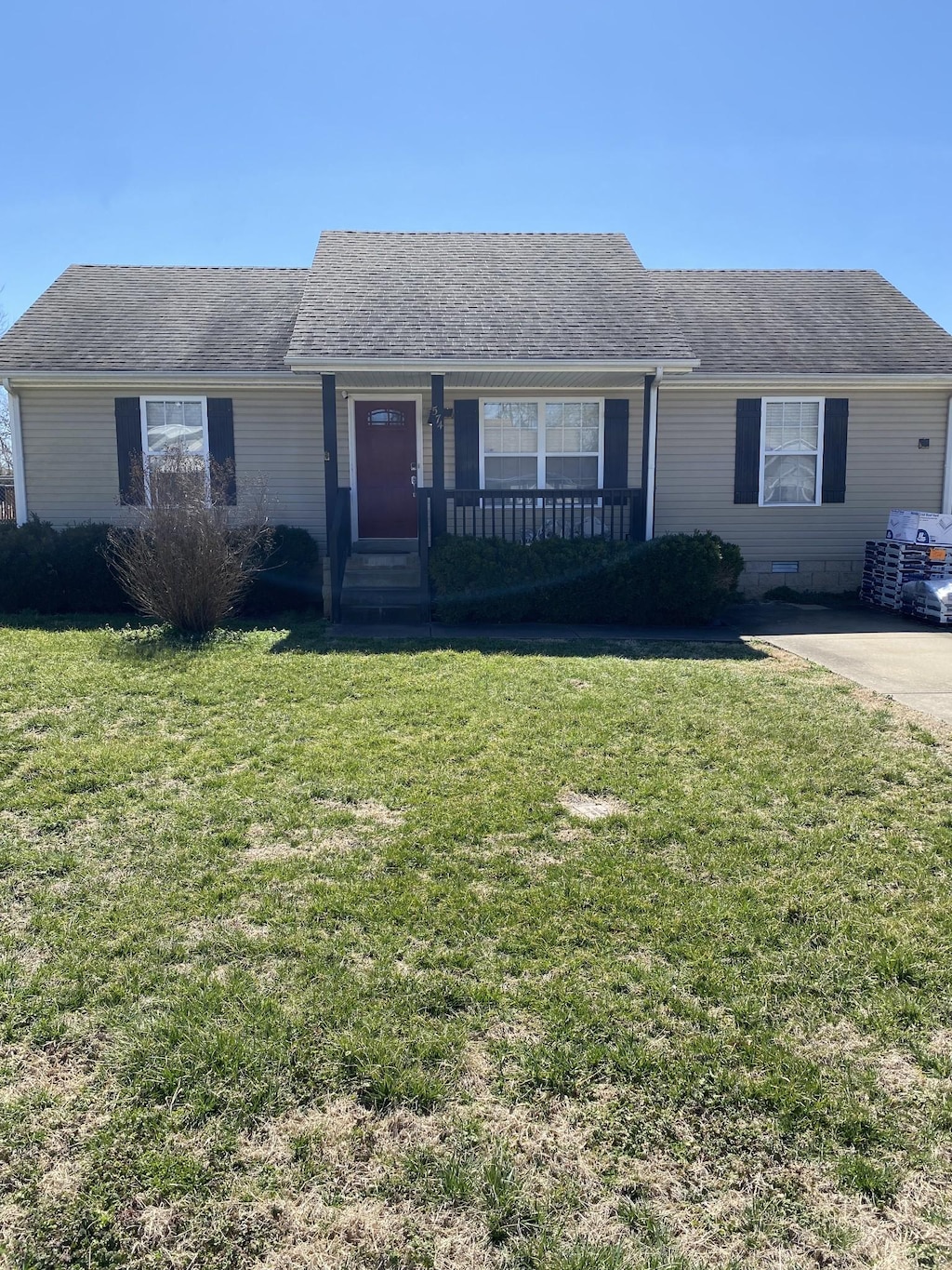 ranch-style house featuring a front yard, covered porch, roof with shingles, and crawl space