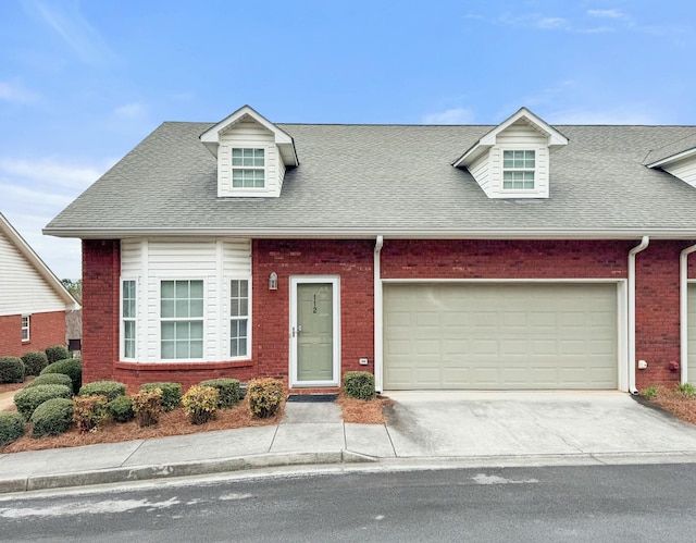 cape cod house with concrete driveway, a garage, brick siding, and roof with shingles