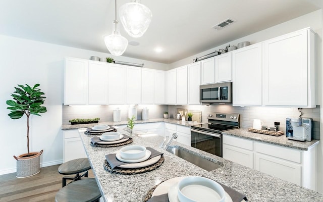 kitchen featuring visible vents, backsplash, light stone counters, appliances with stainless steel finishes, and a sink