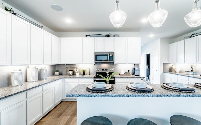 kitchen featuring tasteful backsplash, light wood-type flooring, a kitchen bar, white cabinets, and stainless steel appliances