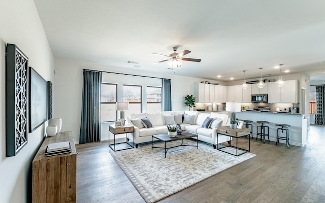 living area featuring visible vents, light wood-style flooring, baseboards, and a ceiling fan