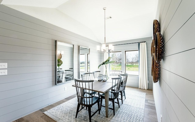 dining area with wooden walls, visible vents, vaulted ceiling, wood finished floors, and a notable chandelier