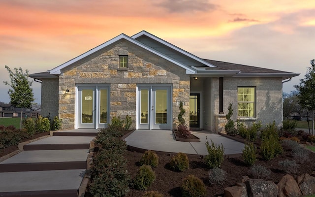 back of property at dusk with stone siding, french doors, and a patio