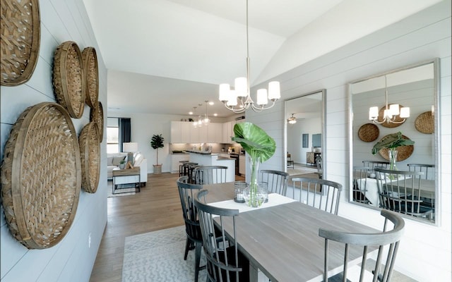 dining space with ceiling fan with notable chandelier, light wood-type flooring, and lofted ceiling