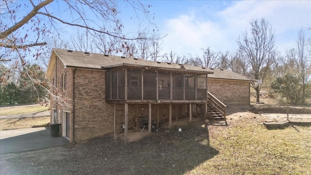 rear view of house with brick siding, an attached garage, stairs, a sunroom, and driveway