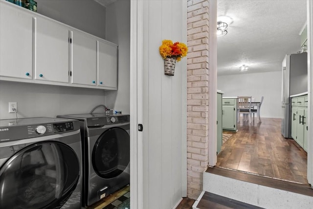 clothes washing area with washer and clothes dryer, cabinet space, dark wood finished floors, and a textured ceiling