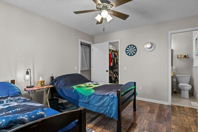 bedroom featuring a spacious closet, baseboards, wood finished floors, ensuite bath, and a textured ceiling