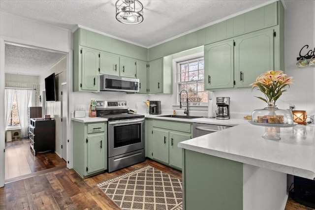 kitchen featuring ornamental molding, a peninsula, a textured ceiling, stainless steel appliances, and a sink