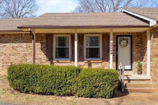 entrance to property featuring brick siding and a shingled roof