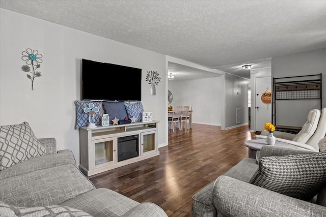 living room featuring visible vents, a textured ceiling, baseboards, and wood finished floors