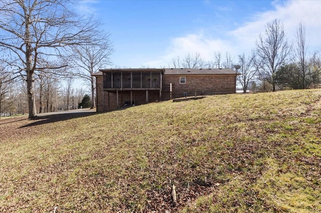 rear view of property with brick siding, a lawn, and a sunroom